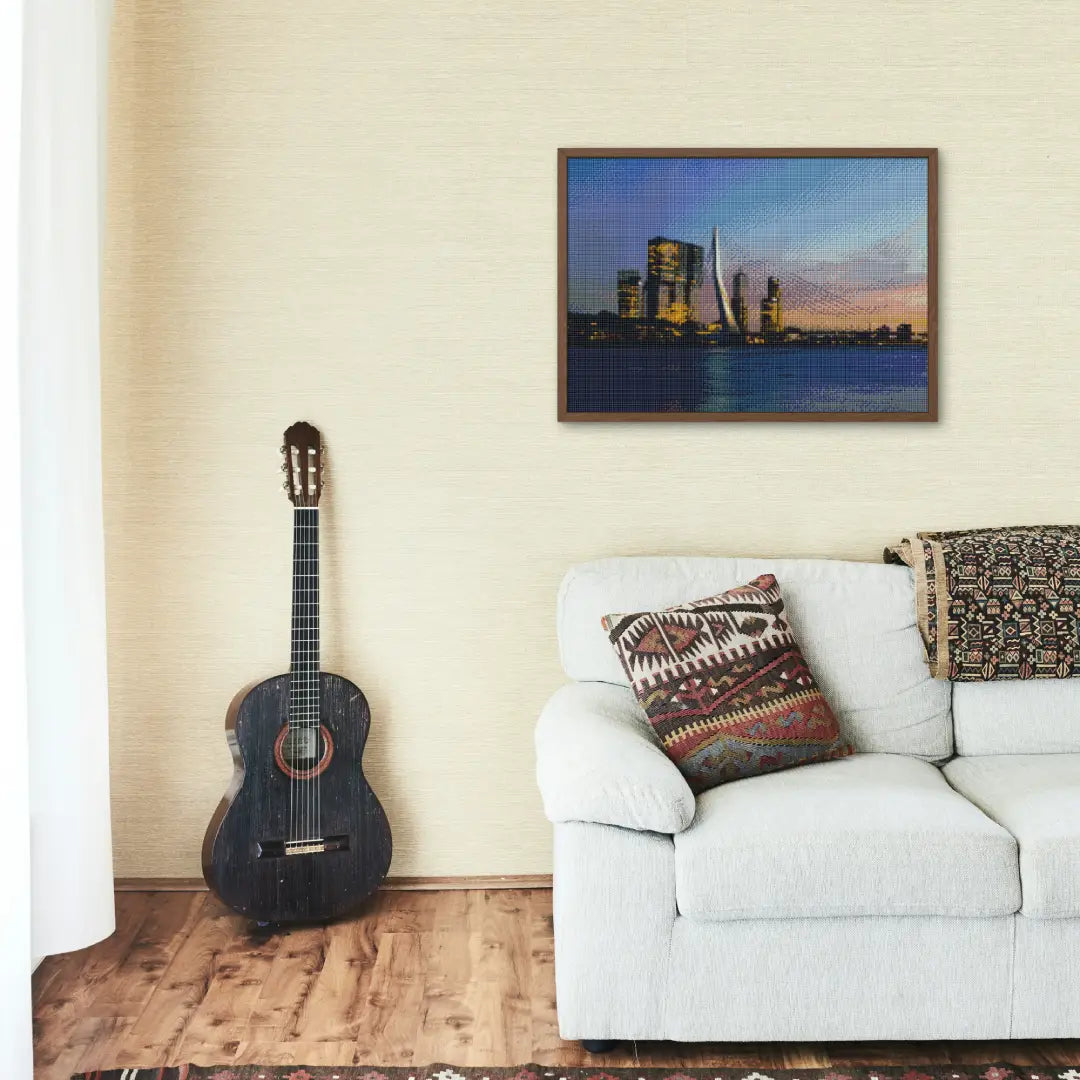 Diamond painting van een skyline van een stad bij zonsondergang, aan de muur boven een witte bank en naast een gitaar.