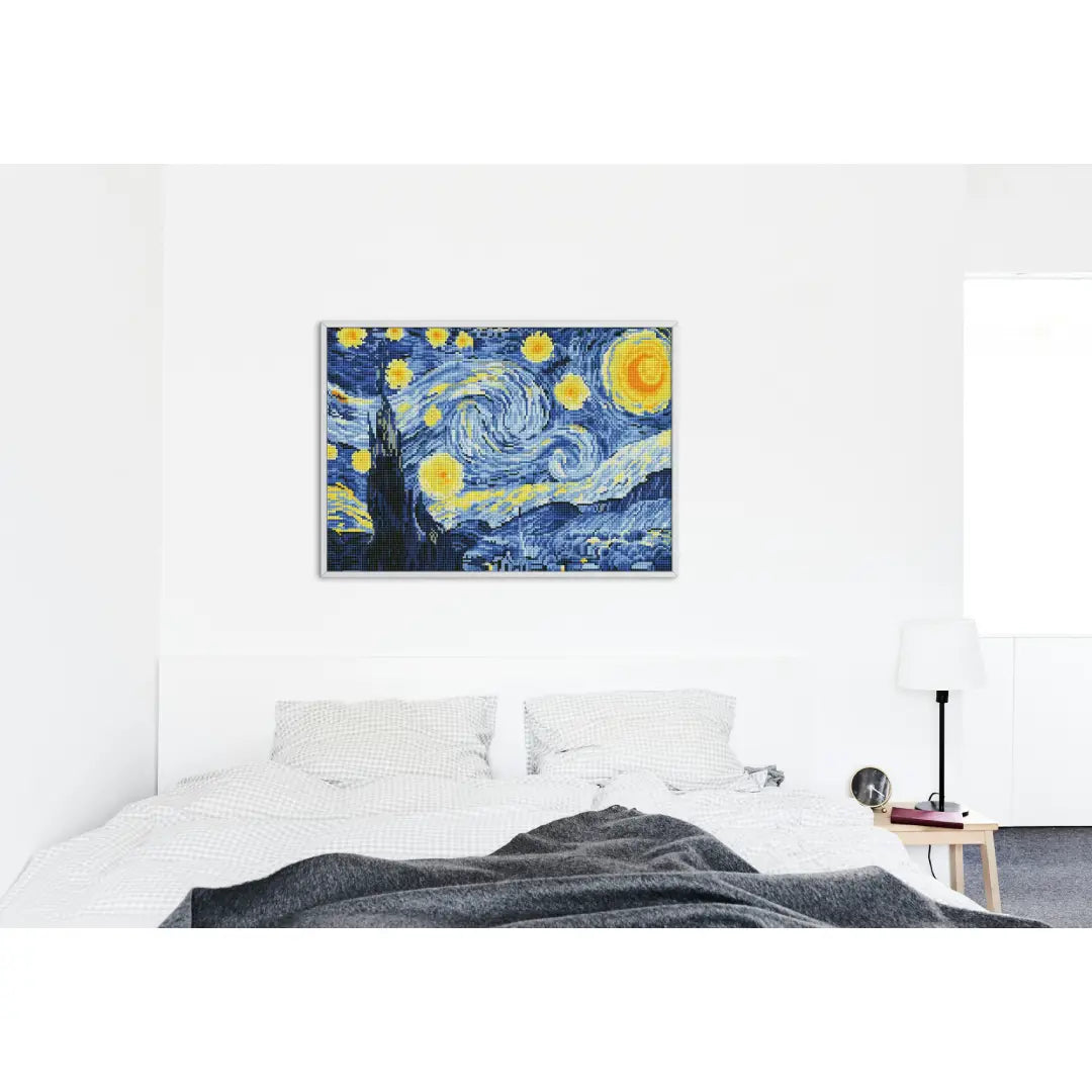 Ingelijst diamond painting van 'De Sterrennacht' boven een wit bed in een minimalistische slaapkamer.