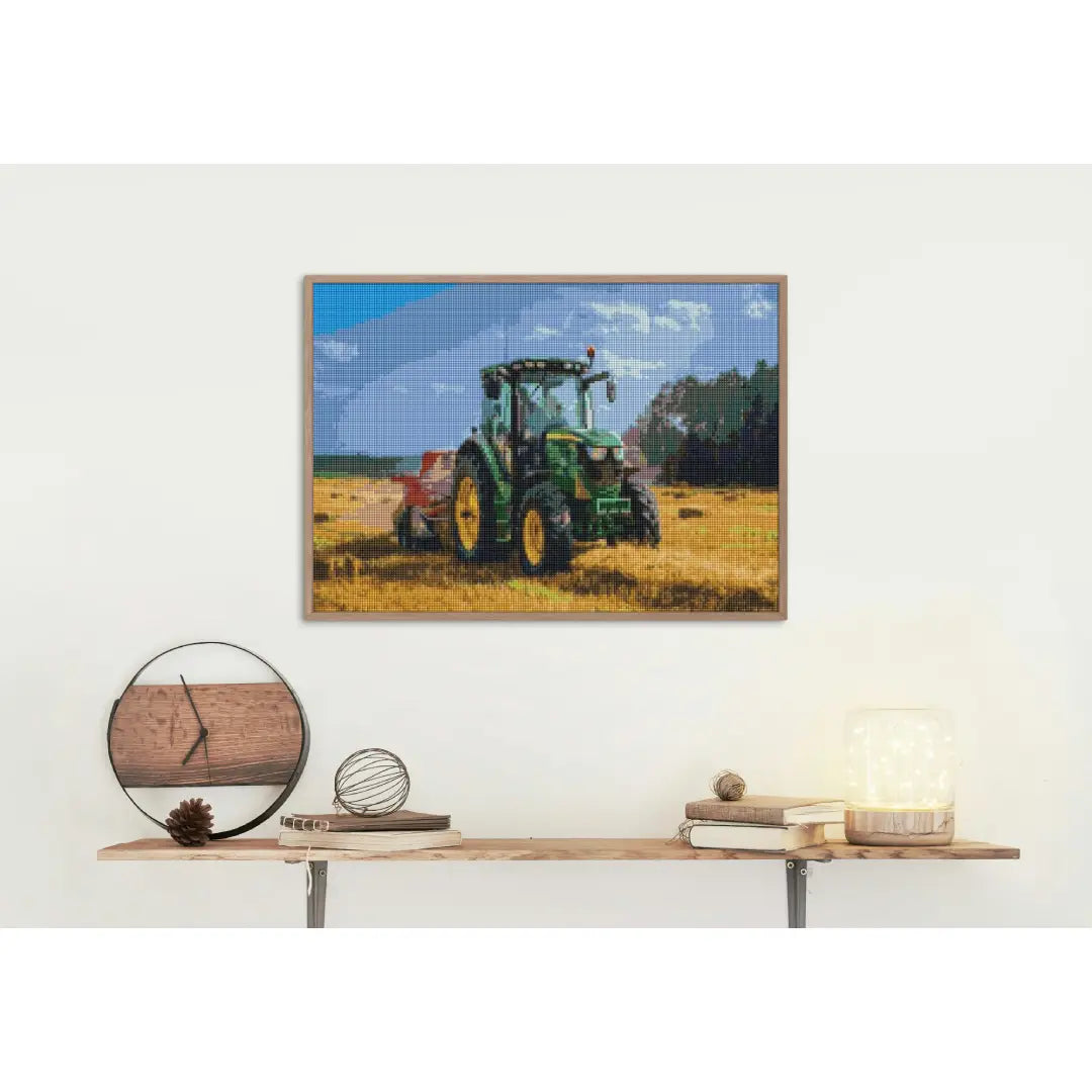 Diamond painting van een groene tractor op een veld onder een blauwe hemel, aan de muur boven een houten plank met boeken en decoratieve items.