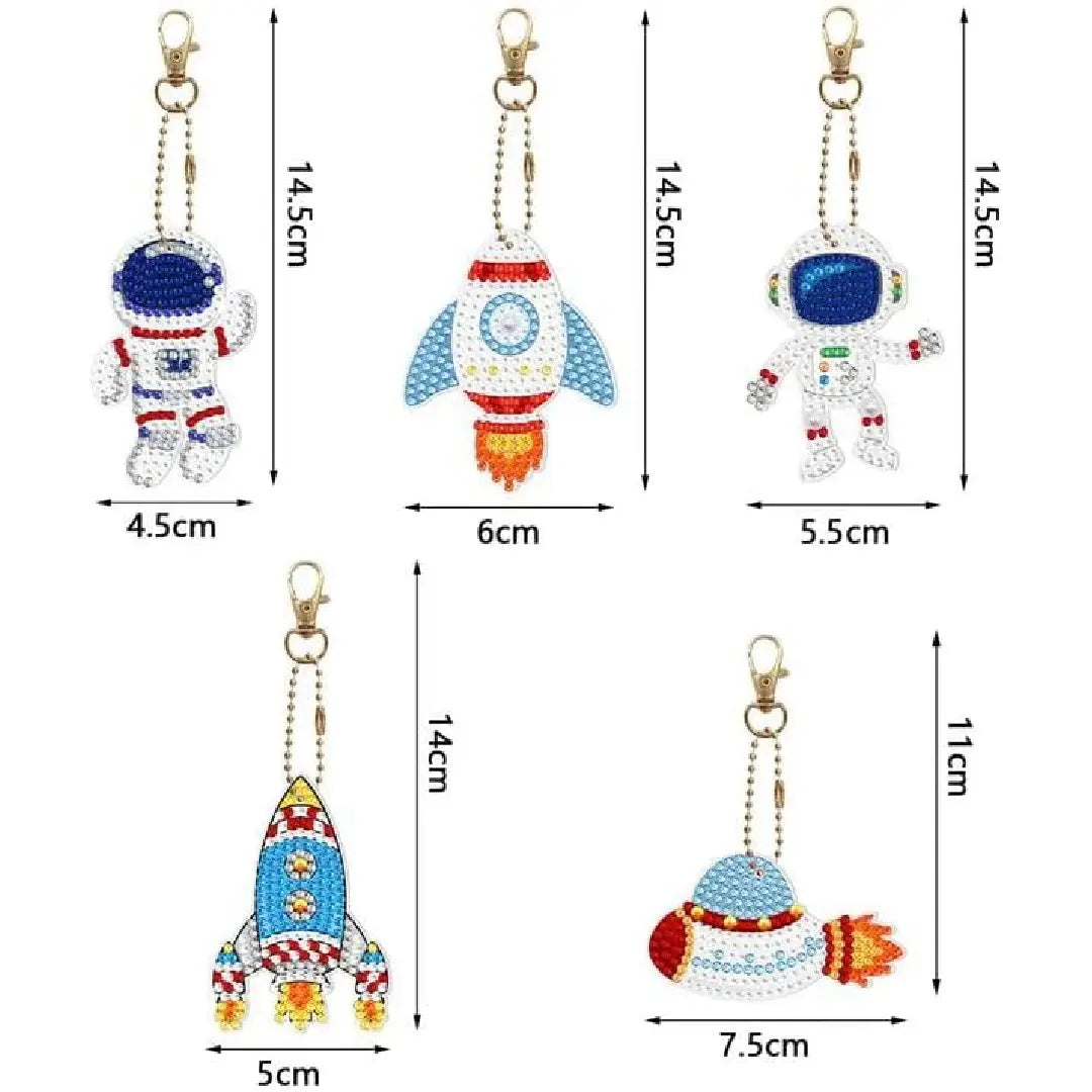 Vijf diamond painting ruimte-thema sleutelhangers, inclusief astronauten en raketten, versierd met kleurrijke details, maten variërend van 4.5 tot 7.5 cm breed en 14.5 cm hoog.