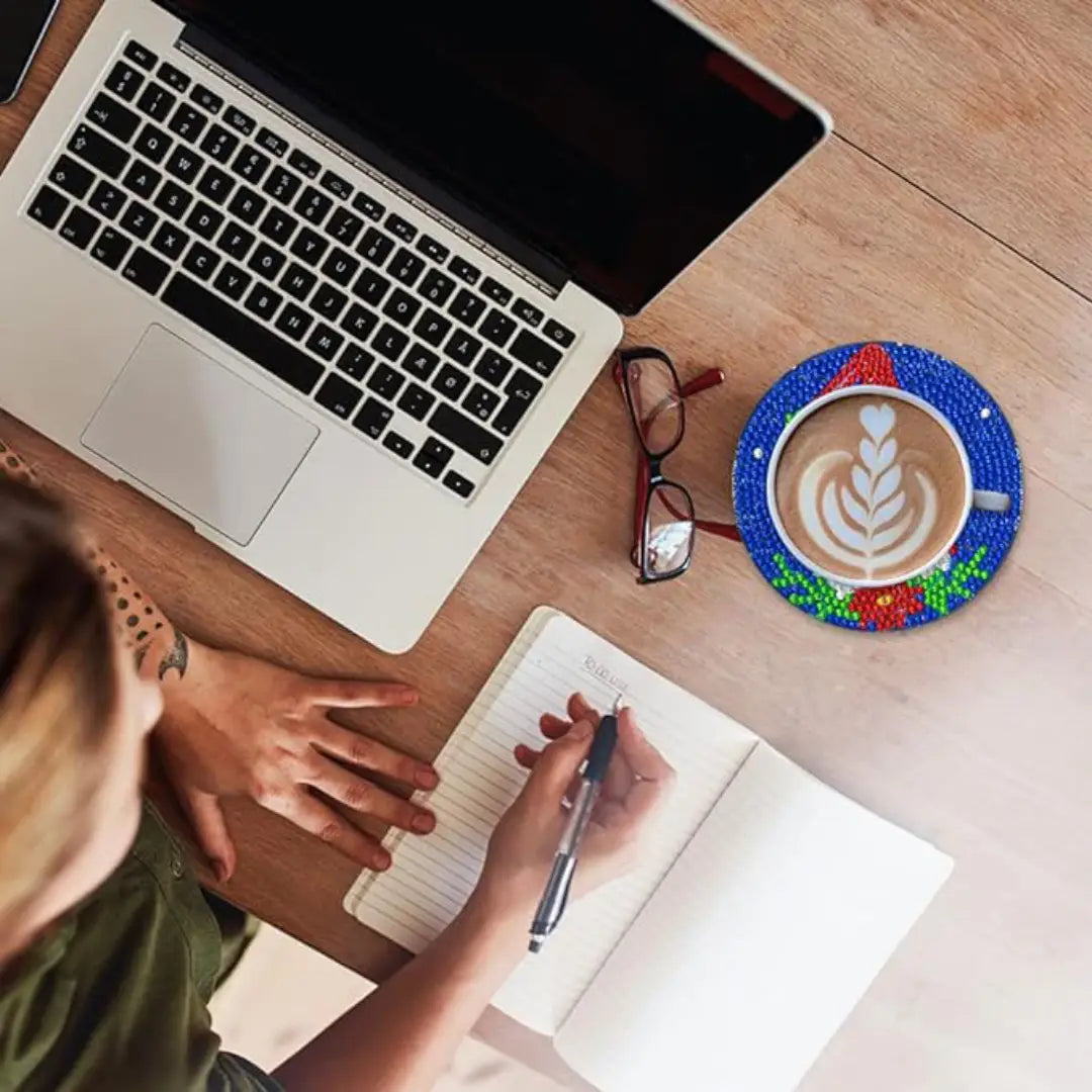 Diamond painting kerstman onderzetter met kop koffie naast een laptop en notitieboekje